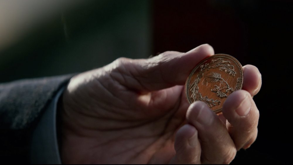 Winston holds a gold coin that serves as a social currency Under the High Table